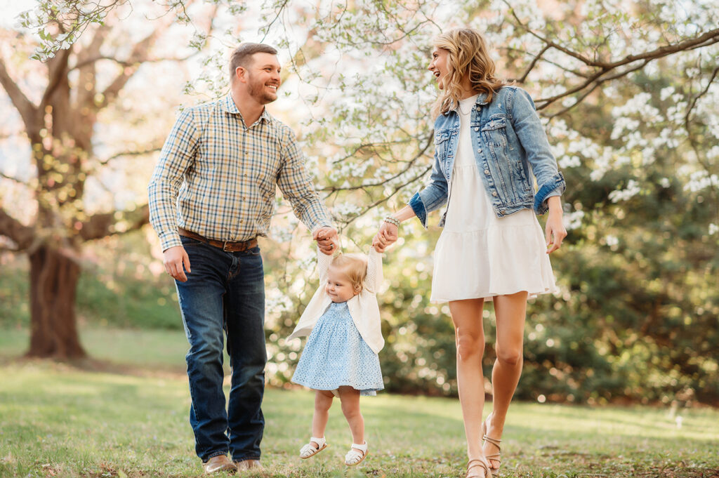 Parents walk with their baby among Dogwood Flowers during a Spring Photoshoot in Asheville, NC.