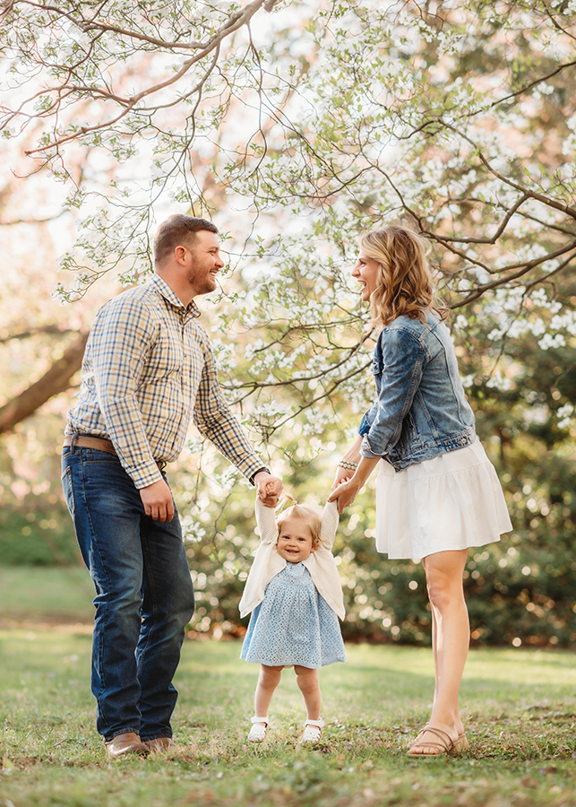 Parents walk with their baby among Dogwood Flowers during a Spring Photoshoot in Asheville, NC.