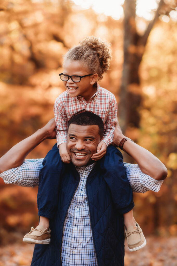 Father gives his young son a piggy back ride through the fall foliage during  Fall Family Portraits on the Blue Ridge Parkway in Asheville, NC.