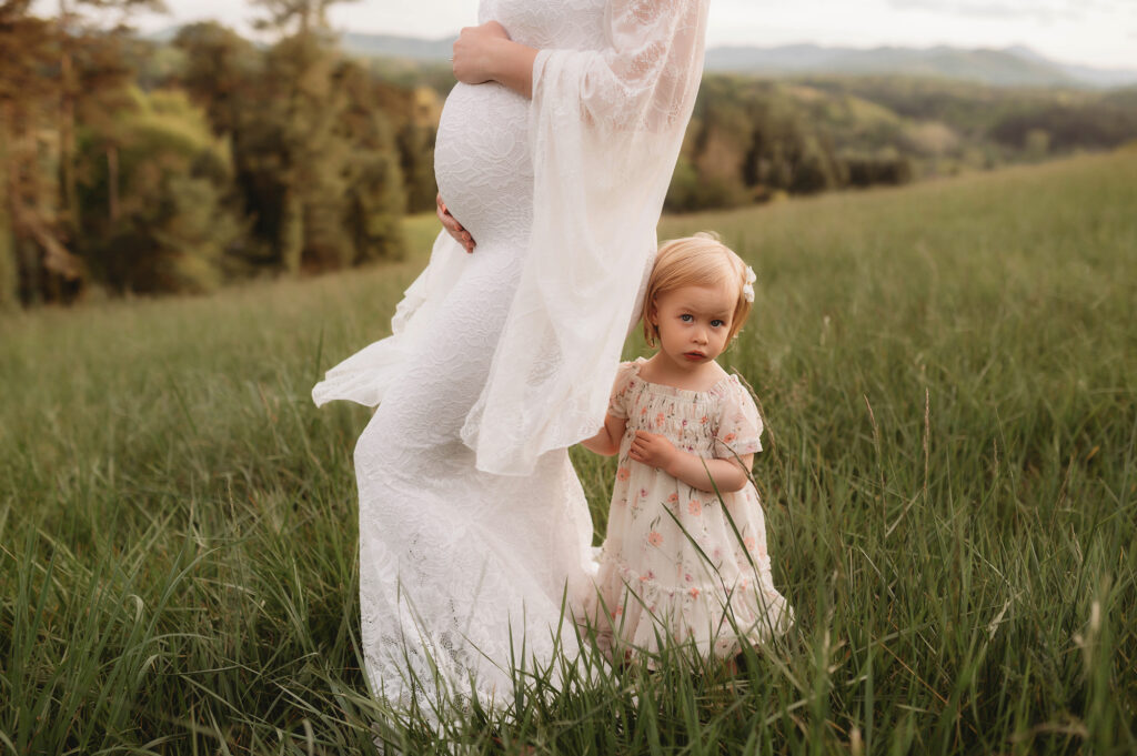 Pregnant woman holds her baby's hand during Maternity Photoshoot at Biltmore Estate in Asheville, NC after explaining Why Asheville Moms Love The Littlest Birds Boutique. 