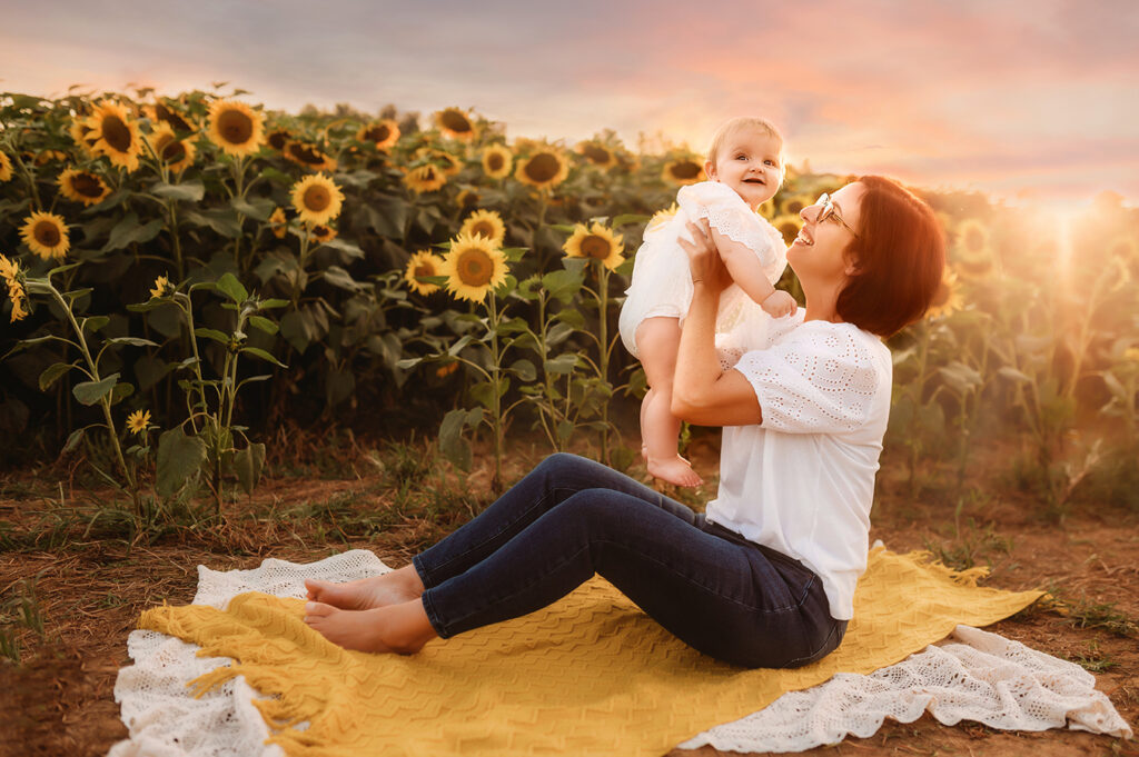 Mother plays with her baby during a Sunflower Field Portrait Session at Biltmore Estate in Asheville, NC.