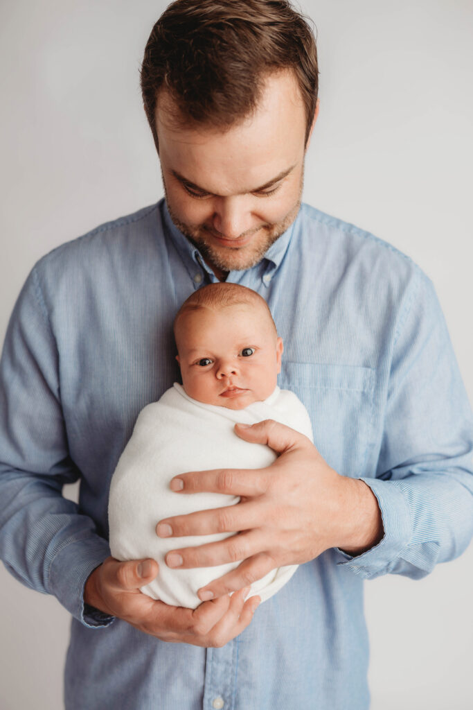 Asheville Newborn Photography Studio provides the Best Newborn Photos in Asheville. Portrait of a Father holding his Newborn Baby boy during his Infant Photoshoot in Asheville.