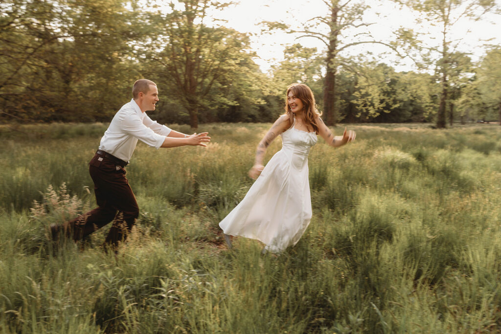 Newly Engaged Couple chases each other through field at Biltmore Estate during their Engagement Photos with Asheville Portrait Company in Asheville, NC