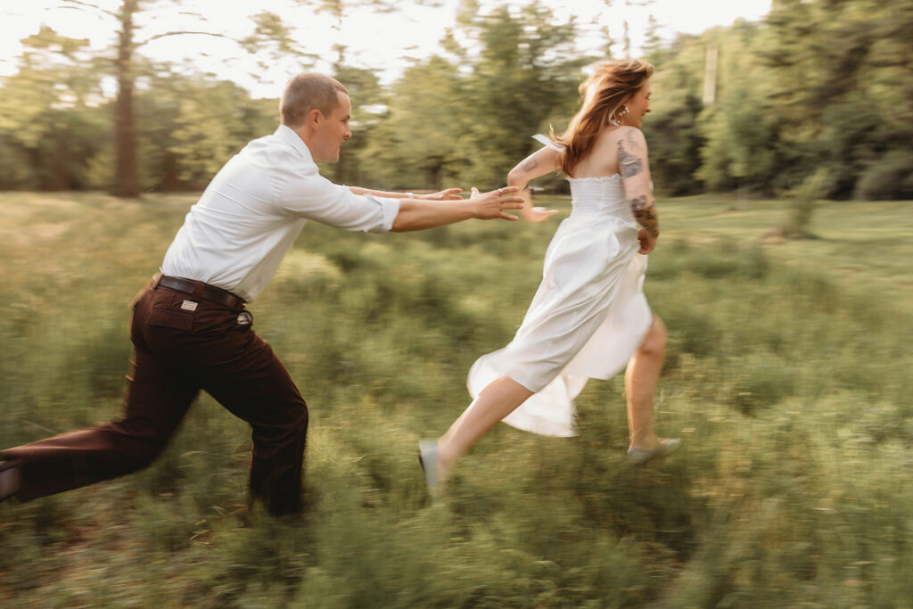 Newly Engaged Couple chases each other through field at Biltmore Estate during their Engagement Photos with Asheville Portrait Company in Asheville, NC