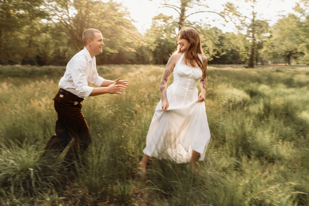 Newly Engaged Couple chases each other through field at Biltmore Estate during their Engagement Photos with Asheville Portrait Company in Asheville, NC
