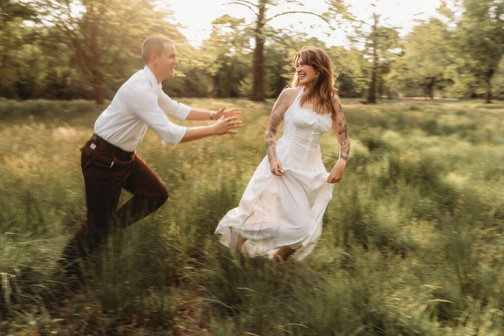 Newly Engaged Couple chases each other through field at Biltmore Estate during their Engagement Photos with Asheville Portrait Company in Asheville, NC